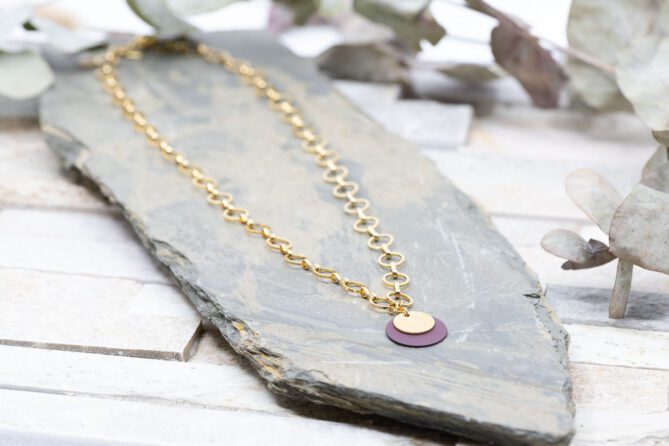 Diese Halskette "Lavender" ist aus Messing und 24k vergoldet. Der Anhänger ist ein violettes Metallplättchen kombiniert mit einer Goldmünze.